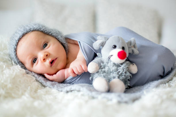 Little newborn baby boy, looking curiously at camera Little newborn baby boy, looking curiously at camera, lay dawn in bed, holding little toy rodent bedding stock pictures, royalty-free photos & images