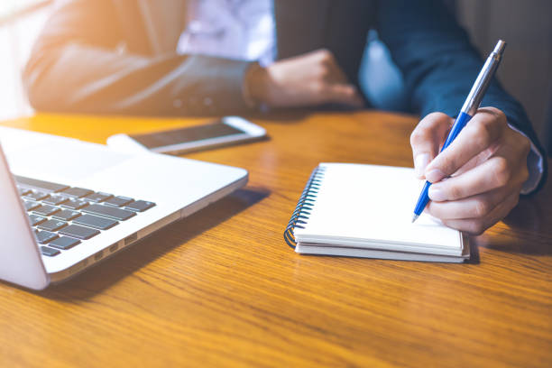 istock business woman hand  using computer laptop and writing on notepad with a pen in office. 858119224