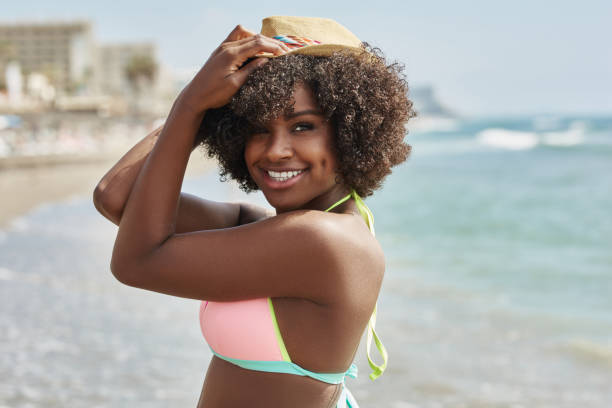 istock Beautiful afro american woman holding hat on head smiling at seaside 858123780