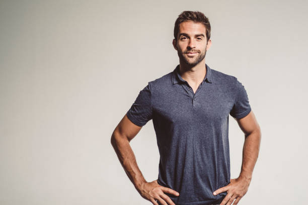 Confident fashionable man standing against gray background. Portrait of handsome mid adult male is with hands on hip. He is wearing casuals.