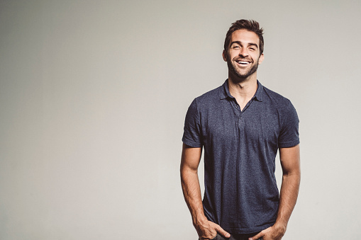 Smiling fashionable man with hands in pockets. Portrait of handsome mid adult male is standing against gray background. He is wearing casuals.