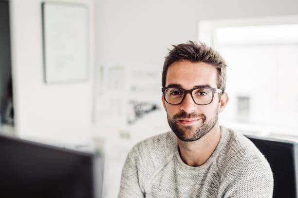 Confident mid adult businessman wearing eyeglasses Portrait of confident businessman wearing eyeglasses. Handsome mid adult professional is sitting at creative office. He is working in bright room. business casual fashion stock pictures, royalty-free photos & images