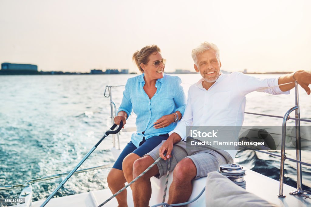 Smiling mature couple enjoying a sunny day sailing together Smiling mature couple sitting together on the deck of their boat while out for a sail on a sunny afternoon Mature Couple Stock Photo