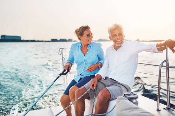 Smiling mature couple enjoying a sunny day sailing together Smiling mature couple sitting together on the deck of their boat while out for a sail on a sunny afternoon sailing couple stock pictures, royalty-free photos & images