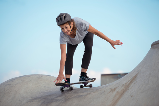 Low angle view of skateboarder senior women traying to keep a balance, skateboarding from a sloping ramp of skateboard pool.