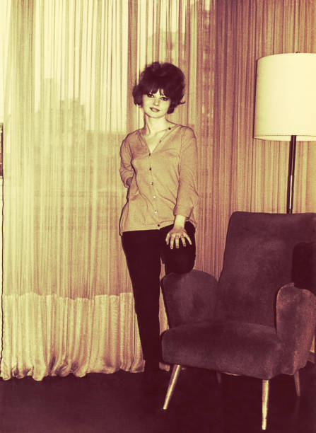 Vintage black and white toned photo from the sixties of a young woman standing in her living room