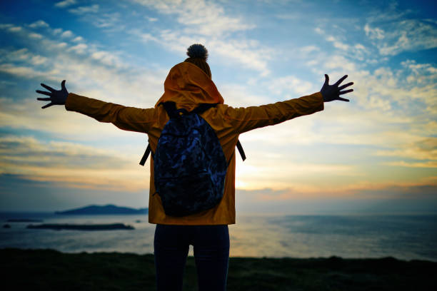 istock Hiker with arms outstretched standing by sea during sunset 858143600