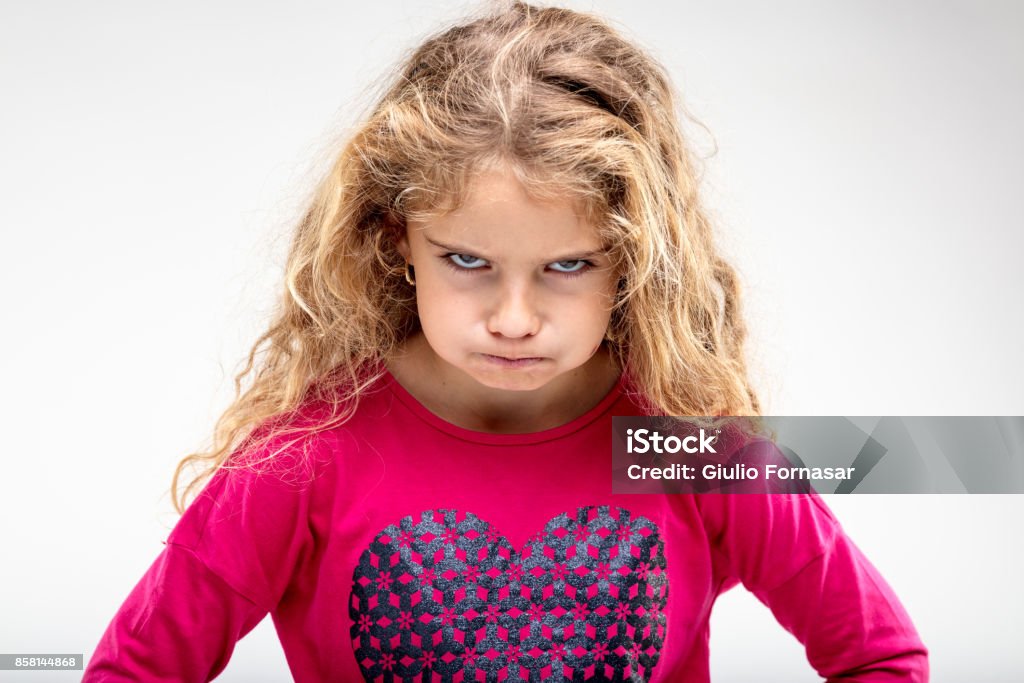 Preteen sulky girl making angry face Portrait of preteen sulky girl making angry face against plain background Child Stock Photo