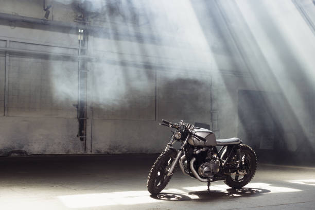 motorcycle standing in dark building in rays of sunlight stock photo
