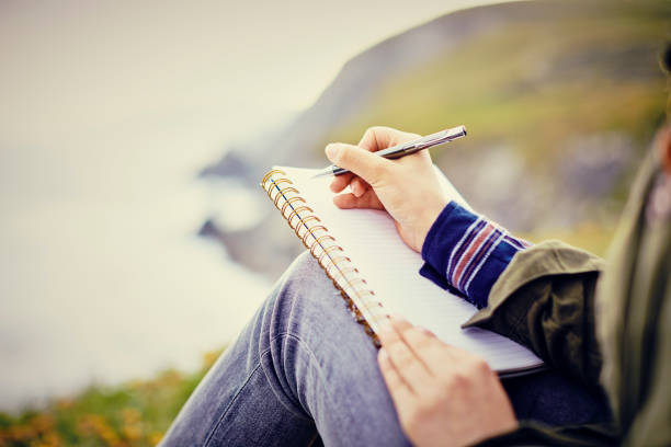 donna che scrive in diario mentre è seduta in montagna - diary writing women human hand foto e immagini stock