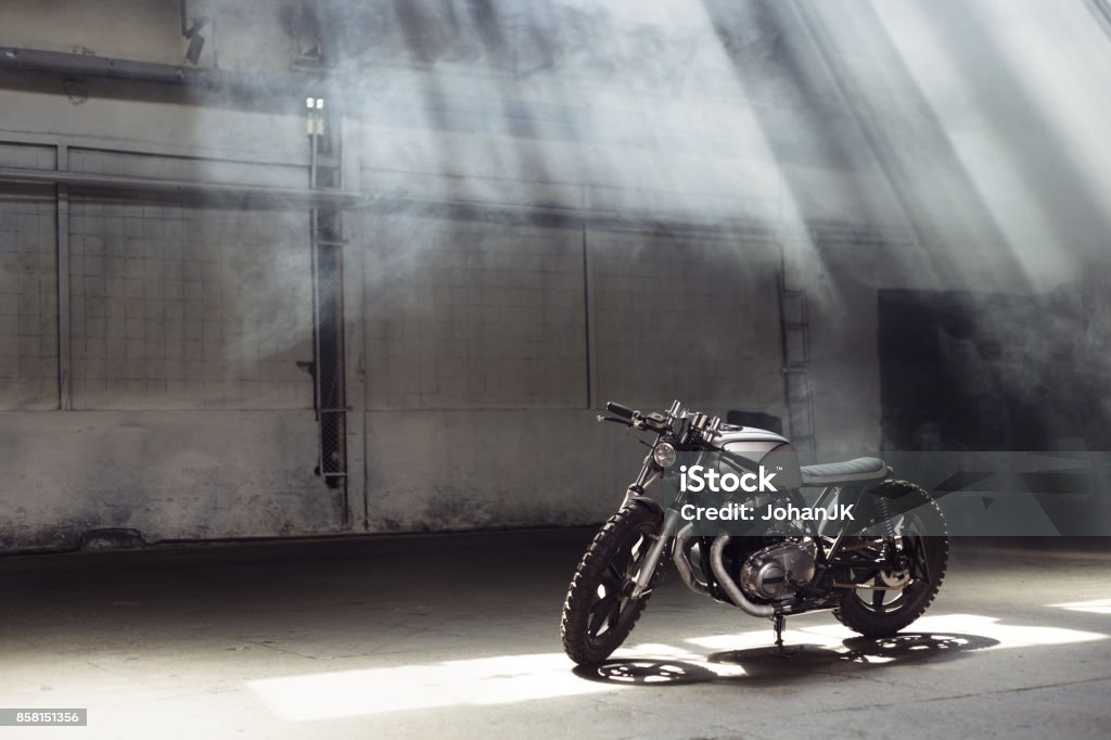 motorcycle standing in dark building in rays of sunlight Vintage motorcycle standing in a dark building in the rays of sunlight. Side view Motorcycle Stock Photo