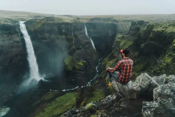 Young Caucasian man sitting  near Haifoss   waterfall in mountains