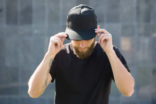 Photo of Hipster handsome male model with beard  wearing black blank baseball cap with space for your logo