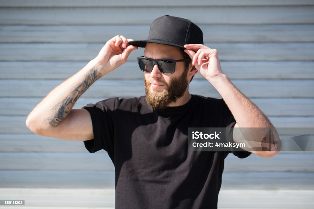 Hipster guapo modelo masculino con el uso de barba negra en blanco gorra con espacio para su logo - Foto de stock de Sombrero libre de derechos