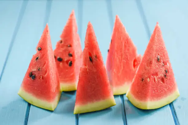 Fresh juicy watermelon with seeds cut into triangles on bright blue background closeup