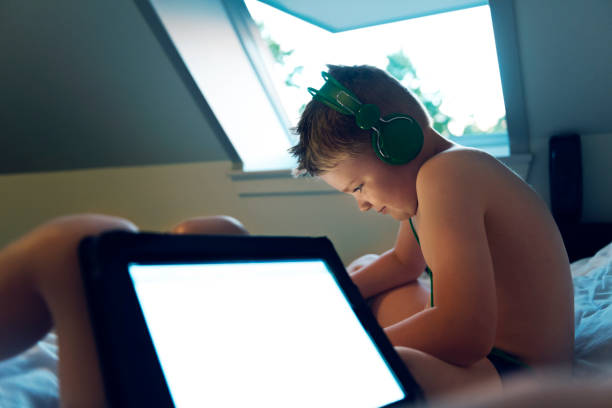 istock Boy sits in bed and plays with his digital tablet while wearing headphones 858180832