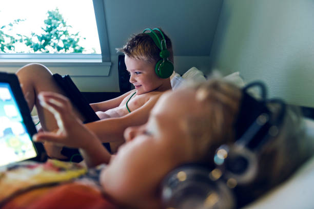もう寝る時間だが、2 人の子供が寝る前に彼らのデジタル錠でコンテンツを観る - gamer video game video computer ストックフォトと画像