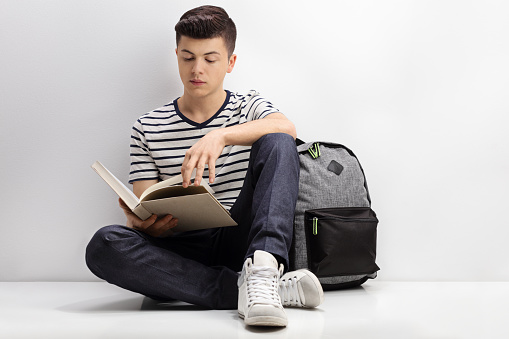 Teenage student reading a book and leaning against a wall