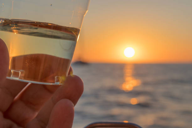 istock Hand grabbing in white wine glass with sunset and ocean view. 858203294