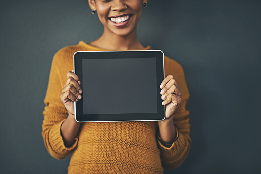 Studio portrait of a young woman holding a digital tablet with a blank screen against a grey background