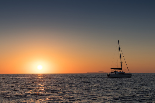 Beautiful sunset in Oia, Santorini, seen from the sea with silhouette of catamaran.