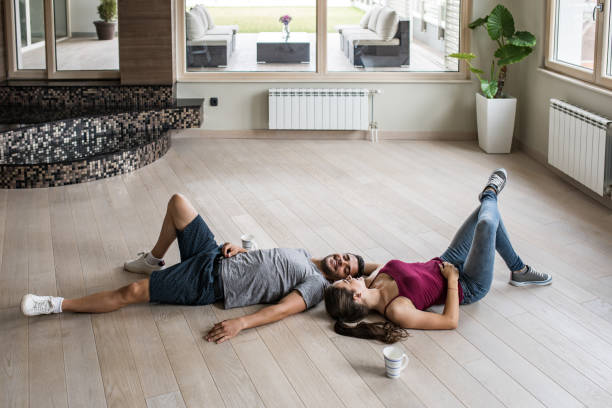 jovem casal feliz relaxante num chão de parquet, em seu novo apartamento. - lying on the floor - fotografias e filmes do acervo