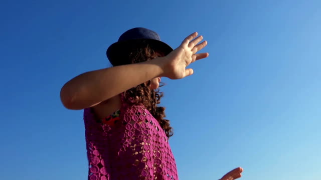 Girl with hat and curly hair dancing at party on the beach