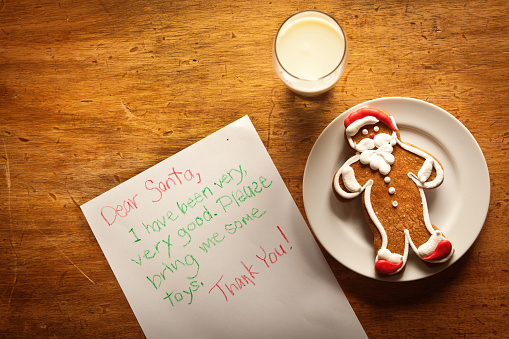 Still life high angle view of a children's letter to Santa Claus together with a Santa cookie on a plate and a glass of milk offering.