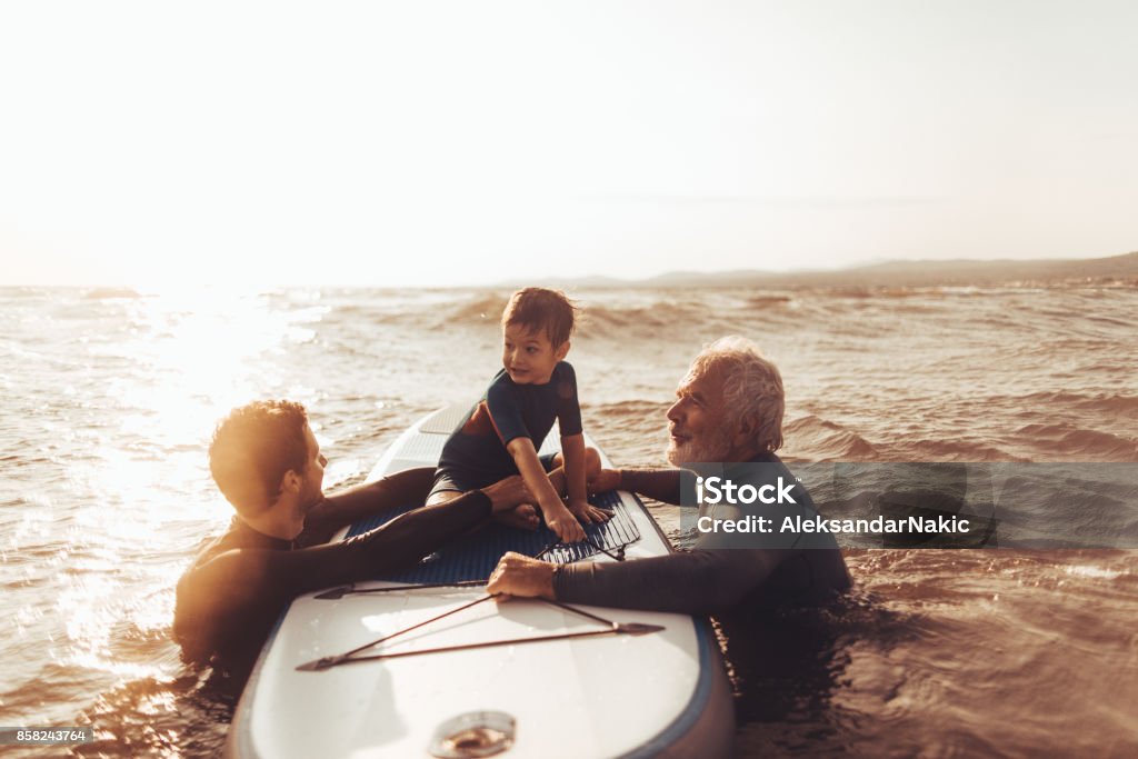 Surfing family Photo of a cheerful little boy getting a surfing lessons from his father and grandfather, both experienced surfers Multi-Generation Family Stock Photo
