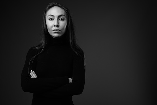 Studio shot of young beautiful woman wearing black long sleeved dress against black background in black and white horizontal shot