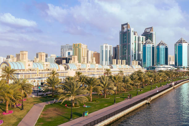 Sharjah downtown skyline Sharjah downtown, with families hanging out along the Khalid Lake corniche's gardens in the afternoon, with the Central Souq and downton's skyscrapers in the background sharjah city stock pictures, royalty-free photos & images