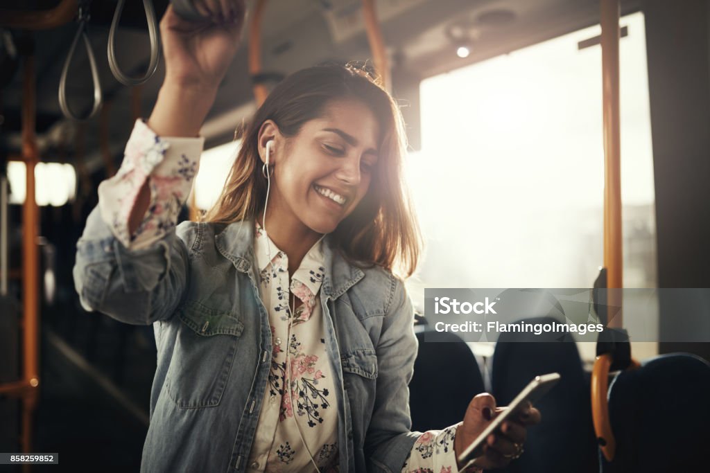 Smiling young woman riding on a bus listening to music Young woman smiling while standing by herself on a bus listening to music on a smartphone Bus Stock Photo