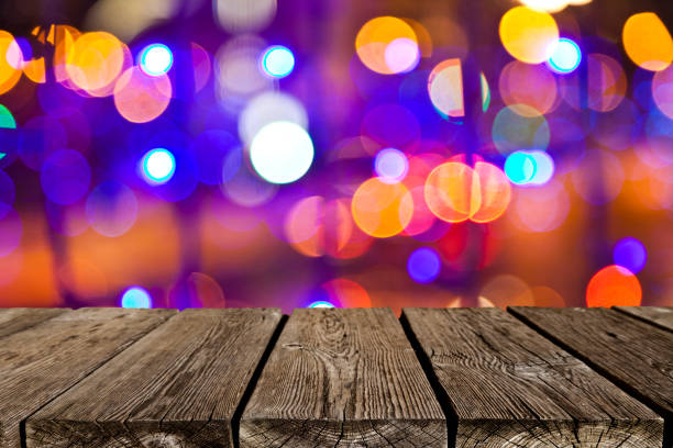 Night view of an empty rustic wooden table in the foreground with defocused colored street lights at background ideal for product or food display. Predominant colors are brown and yellow. DSRL outdoors photo taken with Canon EOS 5D Mk II and Canon EF 24-105mm f/4L IS USM Wide Angle Zoom Lens