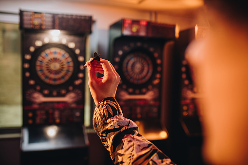 Hand of a man holding dart and aiming while playing darts in entertainment club.