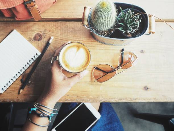 Woman drinking coffee with smart phone and blank notepad on office table