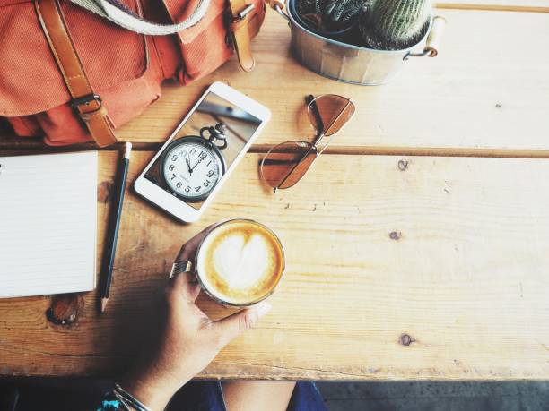 Woman drinking coffee with smart phone and blank notepad on office table