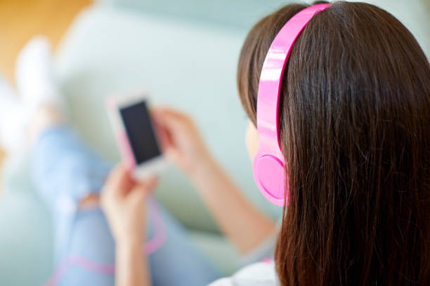 istock Brunette wearing pink headphones while using smart phone at home 858301966