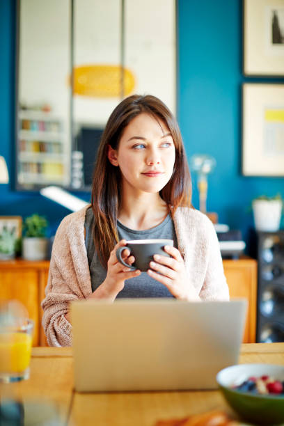 istock Thoughtful young woman with laptop having coffee at home 858302838