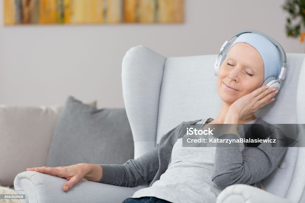 Woman with cancer in armchair Woman with cancer sitting in a blue armchair, wearing big wireless heaphones, and listening to relaxing music Music Stock Photo