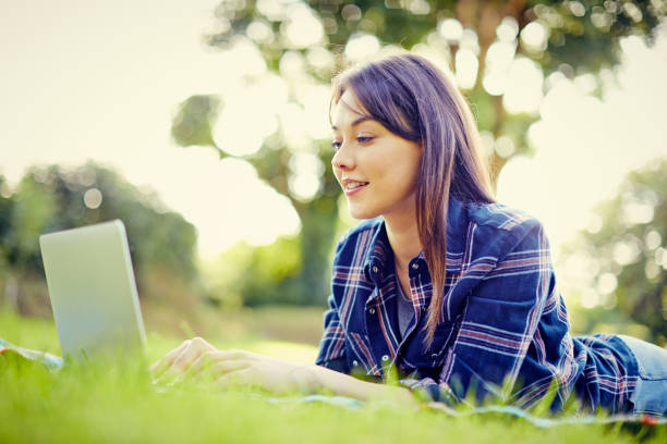 istock Confident young woman using laptop while lying in park 858305728