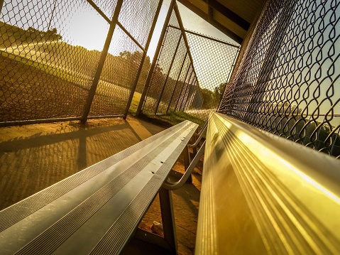 Warm, Angled Photo of a Baseball Dugout at Sunset; with Bleacher Seats, Chain-link Fences and Streaming Sprinklers in the Background