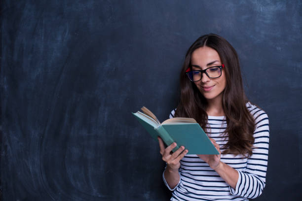 istock Starting to learn more for life. Cheerful young women reading book while standing against blackboard 858327100