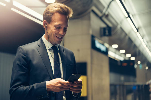 istock Smiling businessman standing in a subway station reading text messages 858341288
