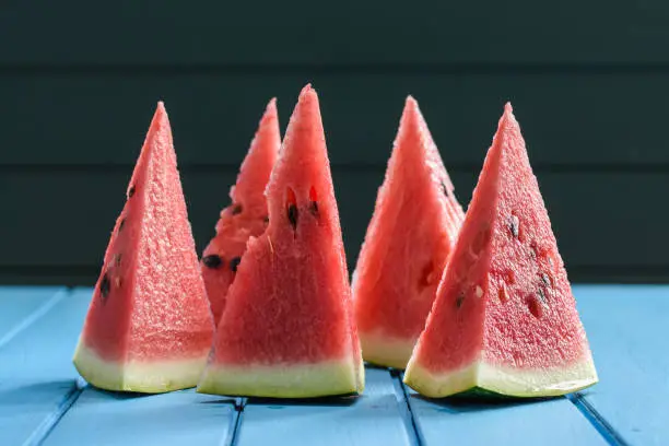 Bright red juicy watermelon cut into high triangles standing on blue table closeup
