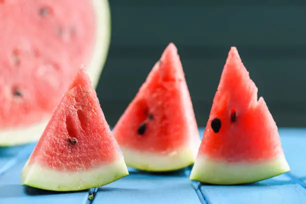Fresh juicy watermelon with seeds cut into triangles on blue background closeup