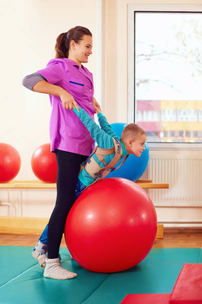 istock cute kid with disability has musculoskeletal therapy by doing exercises in body fixing belts on fit ball 858345880