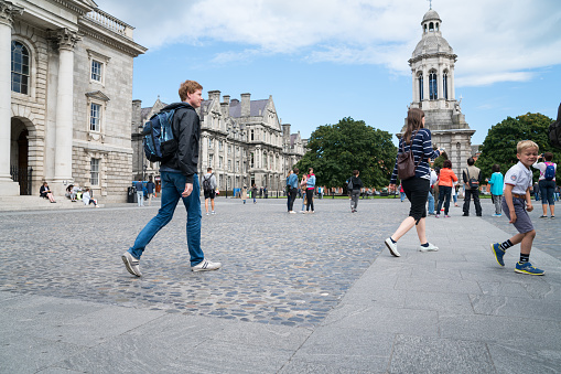 People moving about Parliament Square of Trinity College in grounds and between historic buildings in Dublin in Irish Republic.