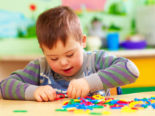 lindo niño con el síndrome de down jugando en el jardín de la infancia - autism fotografías e imágenes de stock
