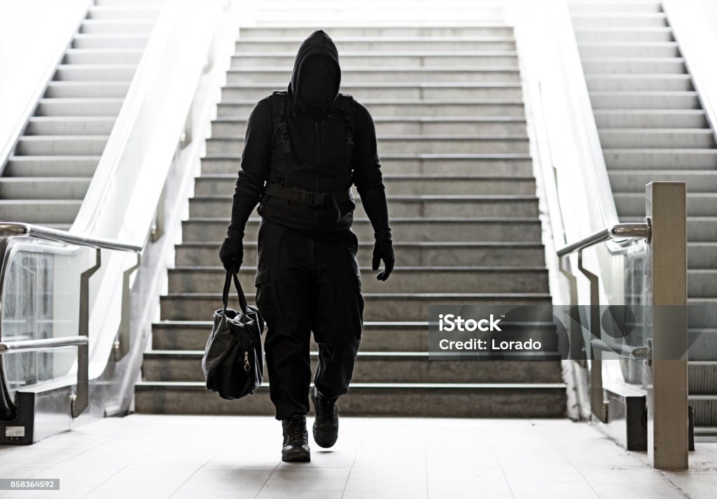 Hooded Lone wolf Man wearing black carrying bag in urban underground public transport setting Terrorism Stock Photo