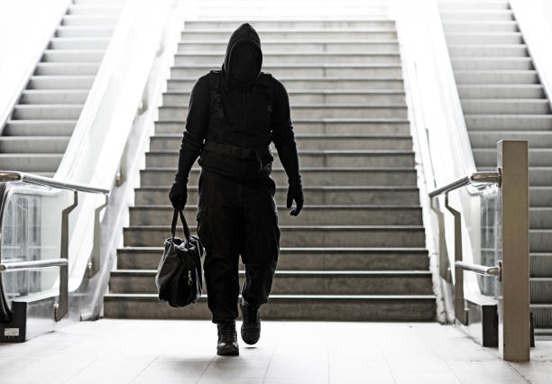 Hooded Lone wolf Man wearing black carrying bag in urban underground public transport setting stock photo
